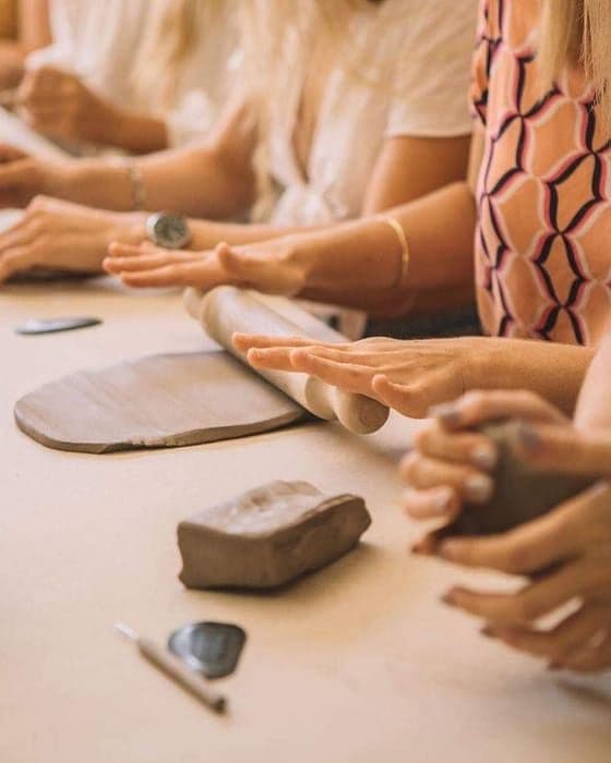 Taller de cerámica con piezas secándose y manos trabajando el barro