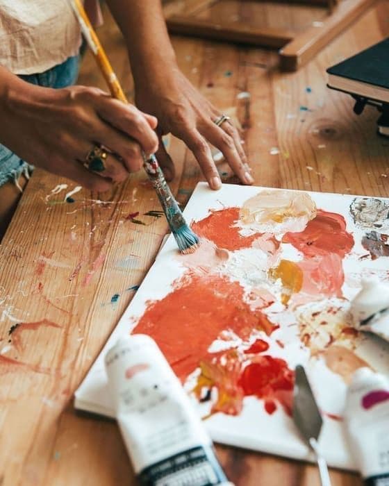 Manos con anillos mezclando pintura roja sobre una paleta